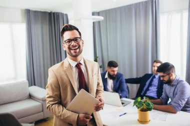 Lider CEO ya da profesyonel işletme koçu arka planda çeşitli mutlu ekiple ofiste poz veren kameraya bakıyor..