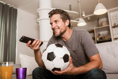 Genç futbol fanatiği oturma odasındaki kanepede futbol maçı izliyor..