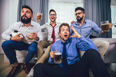 Erkekler televizyonda birlikte spor izleyip neşeli çığlıklar atıyorlar. Bir grup arkadaş kanepede oturup futbol maçı izliyorlar..