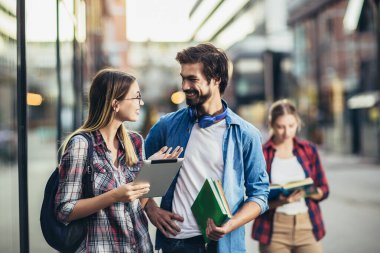 Üniversitede kitaplarla ve dijital tabletlerle okuyan mutlu genç üniversite öğrencileri.