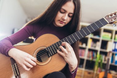 Güzel kız evdeki gitarda yeni bir ses alıştırması yapıyor.