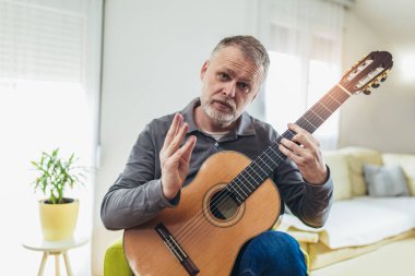 Evde gitar çalarken gülümseyen sıradan giyinmiş yakışıklı bir adam.