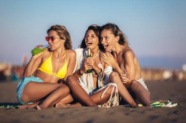 Kumsalda oturan mutlu genç kadınlar. Bir grup arkadaş plaj tatilinde eğleniyor..