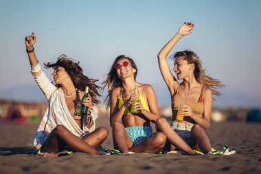 Kumsalda oturan mutlu genç kadınlar. Bir grup arkadaş plaj tatilinde eğleniyor..