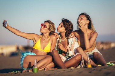 Kumsalda oturan mutlu genç kadınlar. Bir grup arkadaş plaj tatilinde eğleniyor..