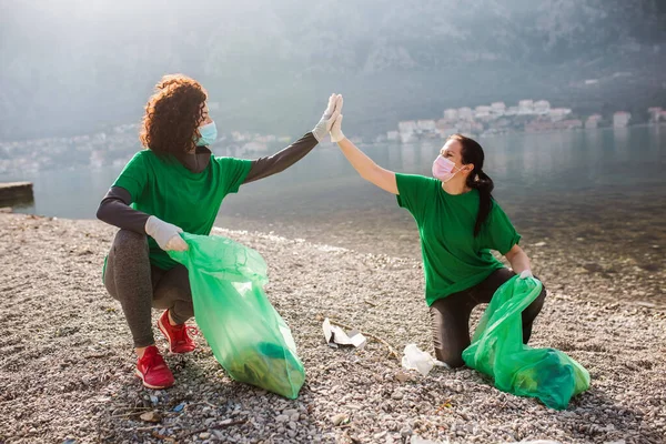 Female volunteers clean beach from garbage, plastic, hold green trash bags and care of environment.