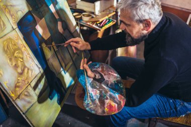 Sanat stüdyosunda tuvale resim yapan olgun bir adam..