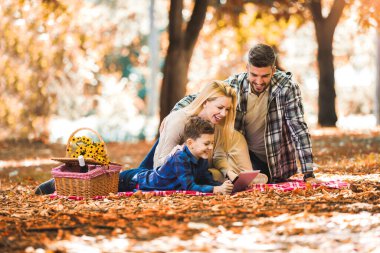 Mutlu aile parkta piknik yapıyor, dijital tablet kullanıyor..