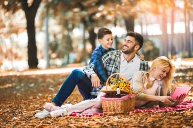 Mutlu aile parkta piknik yapıyor, dijital tablet kullanıyor..