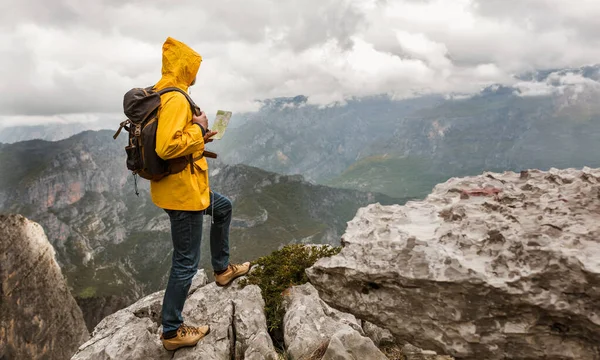 Middle age man traveler in raincoat and backpack enjoying view of mountains.