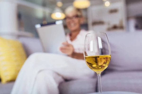幸せな引退したシニア女性は自宅でリラックスします デジタルタブレットを使用して ワイングラスに焦点を当て — ストック写真