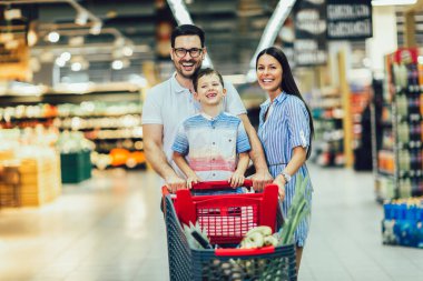 Çocuklu ve alışveriş arabalı mutlu bir aile marketten ya da marketten yiyecek alıyor.