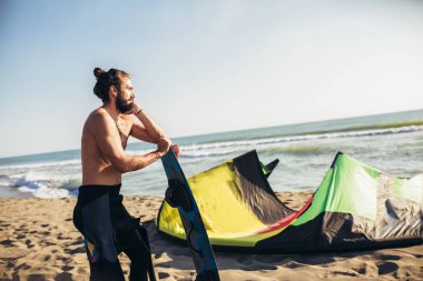 Kumsalda elinde uçurtmasıyla duran profesyonel sörfçü.