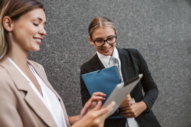 Kafkas kadın asistan iş kadınına tablet cihazında bir şey gösteriyor, konuşuyor ve iş hakkında konuşuyor..