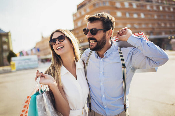 Beautiful couple with shopping bags is talking and smiling while doing shopping in the city