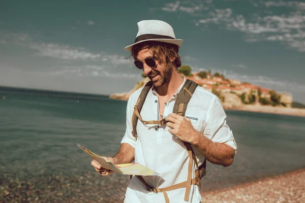 笑顔の観光客の男が地図とバックパックを海の近くに立っている — ストック写真