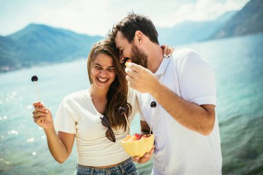 Kumsalda meyve yiyen genç çift kumsalda eğleniyor.