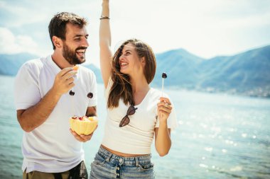 Kumsalda meyve yiyen genç çift kumsalda eğleniyor.