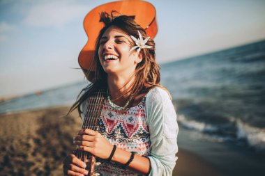 Gün batımında plajda gitar çalan genç bir kadın.