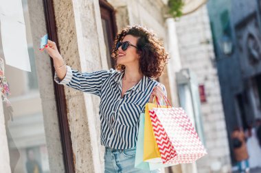 Mutlu kıvırcık saçlı kadın kredi kartıyla alışveriş yapıyor..