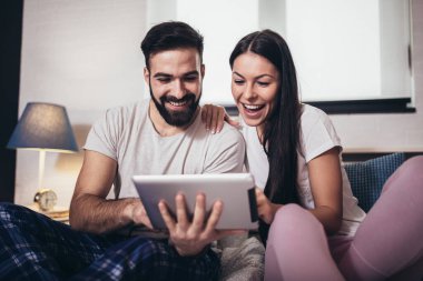 Genç bir çift, bir otel odasında yatarken tablet kullanıyor..