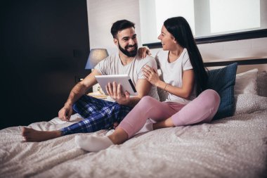 Genç bir çift, bir otel odasında yatarken tablet kullanıyor..