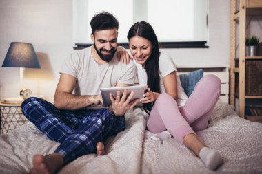 Genç bir çift, bir otel odasında yatarken tablet kullanıyor..