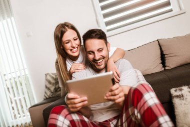 Genç bir çift, oturma odasındaki kanepede oturup internetten medya içeriğini izliyor..