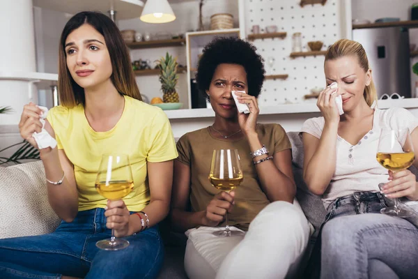 Three female friends watch sad movie at home in sofa crying touching.