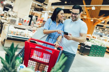 Alışveriş arabasıyla markette yürürken gülümseyen mutlu genç çift.