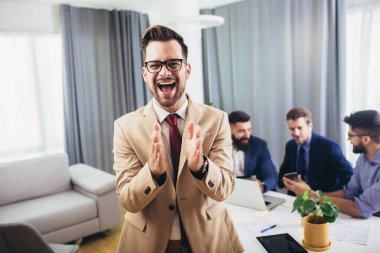 İş adamı lideri, arka planda iş adamları çalışırken modern ofiste kameraya bakıyor.. 