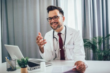 Kendine güvenen doktor büro masasında oturuyor ve çalışıyor.