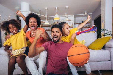 Mutlu Afro-Amerikan ailesi televizyon seyrediyor ve evdeki kanepede basketbol maçlarına tezahürat yapıyor..
