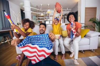 Mutlu Afro-Amerikan ailesi evdeki oturma odasında ragbi maçı izliyor.