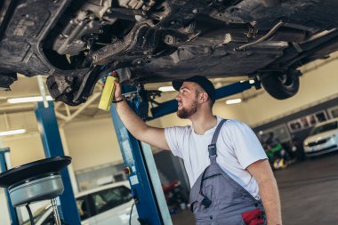 Benzin istasyonunda asansörde asılı duran arabanın yanında profesyonel biri var.