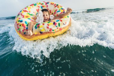 Neşeli çocuk kırılma dalgasında şişirilebilir halka sürüşünde. Seyahat yaşam tarzı, yüzme aktiviteleri. Seçici odak