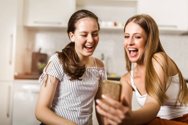 İki neşeli kız evde otururken selfie çekiyor.