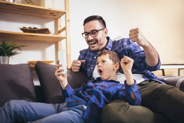 父と息子は家で一緒に時間を過ごしながらスマホゲームや笑顔を使っています — ストック写真