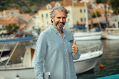 Deniz kenarında tablet bilgisayar tutan yakışıklı bir emeklinin portresi.