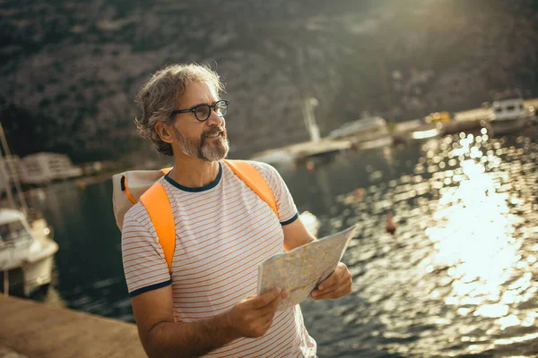 笑顔の観光客成熟した男立って地図と海の近くのバックパック — ストック写真