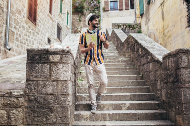 Sırt çantalı mutlu turist şehir genelinde seyahat ederken oryantasyon için bir harita kullanıyor.