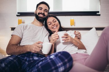 Genç mutlu çift sabahları yatakta kahve içiyor.