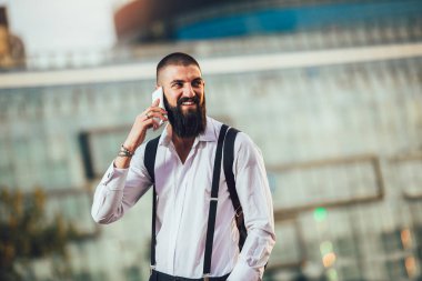 Genç sakallı iş adamı dışarıda telefonla konuşuyor.