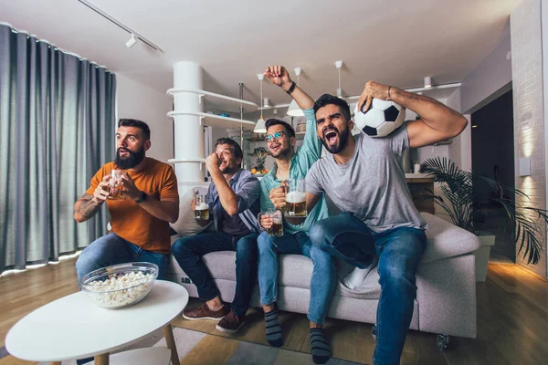 家で一緒にテレビでスポーツを見ている男性は陽気に叫んでいる ソファに座ってサッカーの試合を見ている友人のグループ — ストック写真