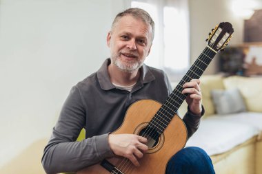 Evde gitar çalan yaşlı bir adam.