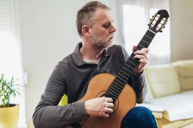 Evde gitar çalan yaşlı bir adam.