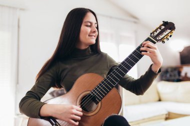 Genç bir kız evdeki gitarda yeni bir ses üzerinde çalışıyor.