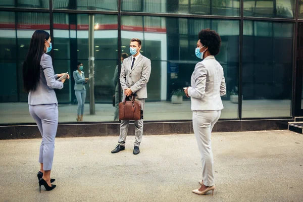 Three employers standing in social distance wearing face mask looking at each other and talking