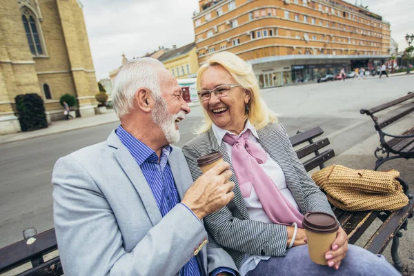 Happy senior couple drinking coffee on a bench in the city