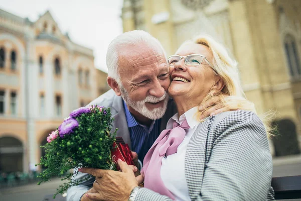 Beautiful senior couple dating outdoors. Man giving his wife present and flowers.